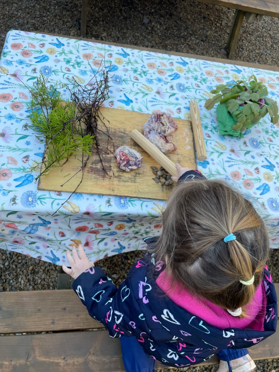 A child seen from above exploring natural materials at an outdoor camp table