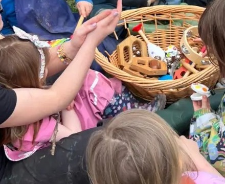 A basket of wooden instruments surrounded by children’s hands during an outdoor camp music session